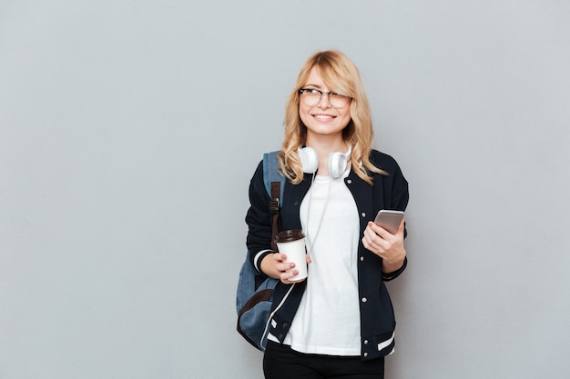 Jeune étudiante tenant une tasse de café et smartphone