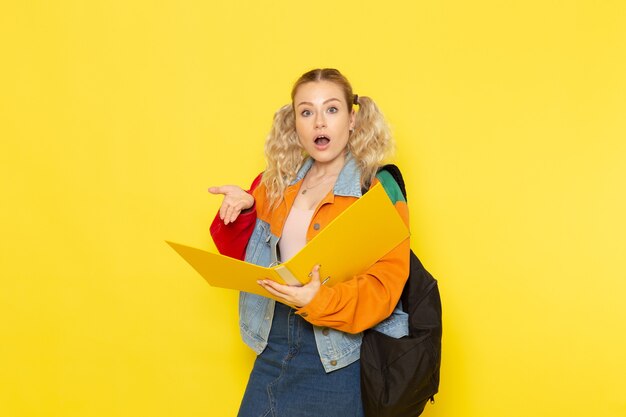 Jeune étudiante en vêtements modernes lecture de fichier sur jaune