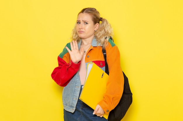Jeune étudiante en vêtements modernes posant simplement avec une expression confuse sur jaune