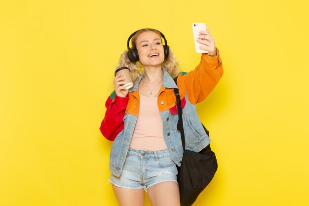 Jeune étudiante en vêtements modernes prenant un selfie sur jaune