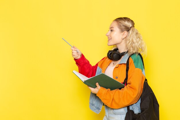 Jeune étudiante en vêtements modernes tenant un cahier vert sur jaune