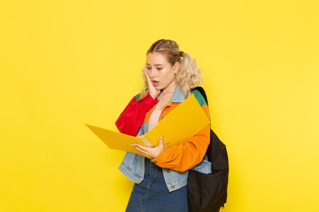 Jeune étudiante en vêtements modernes vérifiant le fichier sur jaune