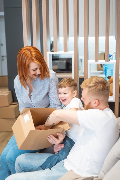 Jeune, famille heureuse, à, gosse, déballage, boîtes, ensemble, s'asseoir sofa