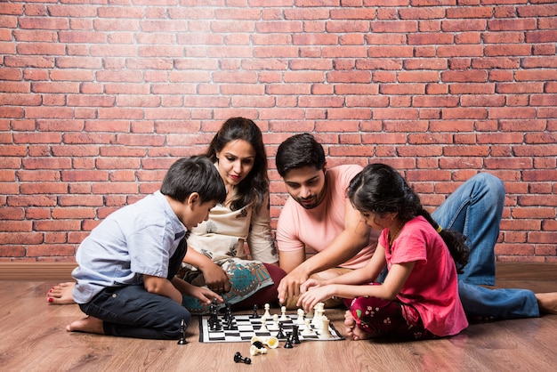 Jeune famille indienne de quatre personnes jouant à des jeux de société comme chess, ludo ou snack and ladder à la maison en quarantaine