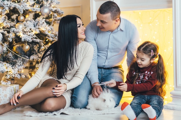 Jeune famille pose devant un sapin de Noël brillant dans une chambre de luxe confortable