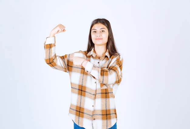 Jeune femme adorable en vêtements décontractés posant sur un mur blanc.