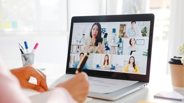 Une jeune femme d'affaires asiatique utilisant un ordinateur portable parle à un collègue du plan lors d'une réunion par appel vidéo pendant qu'elle travaille à domicile dans le salon.