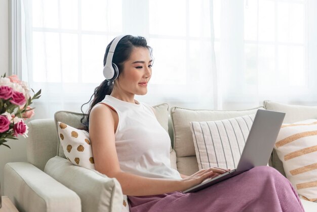 jeune femme d'affaires asiatique utilisant un ordinateur portable tout en se relaxant sur un canapé à la maison travail à domicile