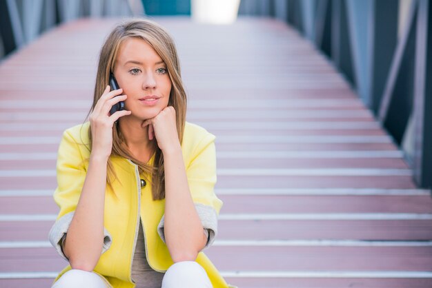 Jeune femme d&#39;affaires, avoir une conversation en utilisant un téléphone intelligent sur un appel téléphonique pendant que vous êtes assis sur le pont