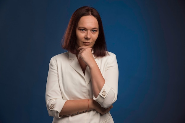 Jeune femme d'affaires en blazer blanc pensant.