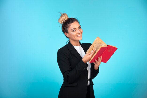 Jeune femme d'affaires en blazer noir tenant un carnet de tâches et se sent positif.