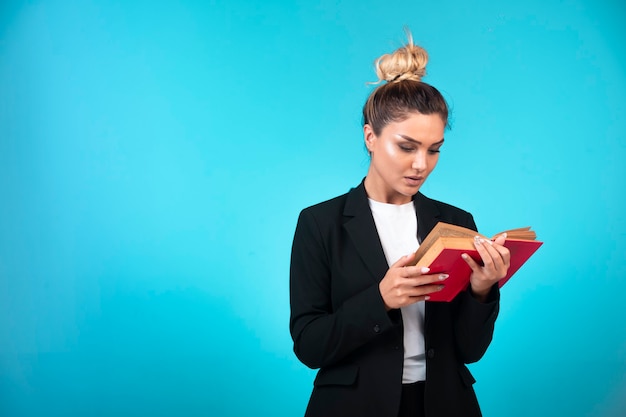 Jeune femme d'affaires en blazer noir tenant un livre de tâches et le lire.