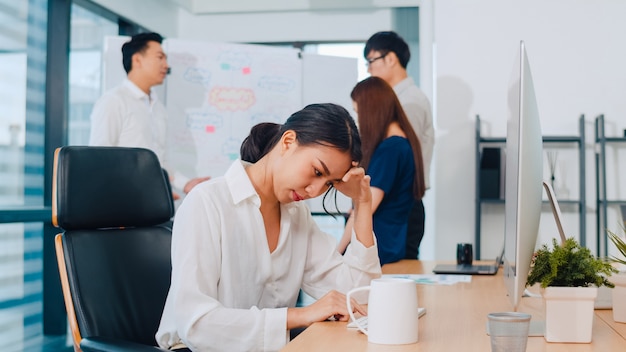 Jeune femme d'affaires chinoise millénaire travaillant stress avec problème de recherche de projet sur le bureau de l'ordinateur dans la salle de réunion au petit bureau moderne. Concept de syndrome d'épuisement professionnel des personnes en Asie.