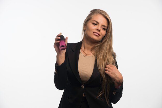 Jeune femme d'affaires en costume noir applique le parfum.