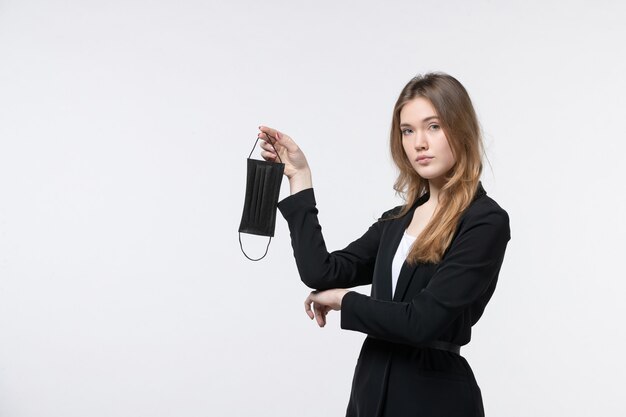 Jeune femme d'affaires en costume tenant un masque médical et posant sur un mur blanc isolé