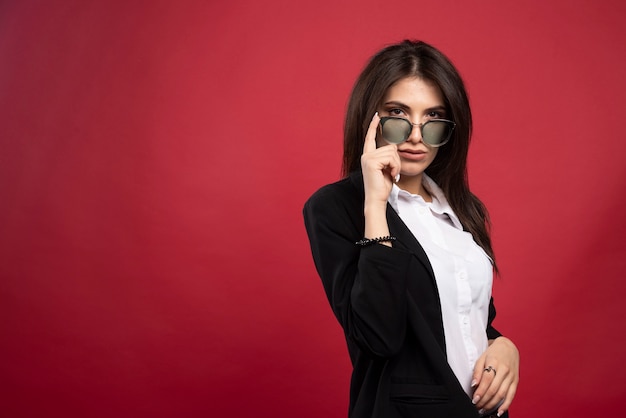 Jeune femme d'affaires debout avec des lunettes sur fond rouge.