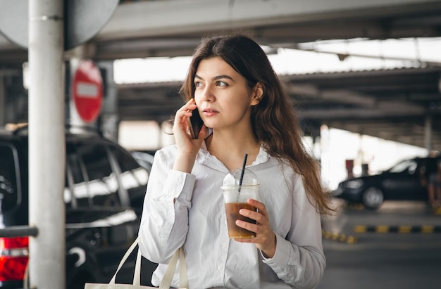 Jeune femme d'affaires avec du café parlant au téléphone dans le parking