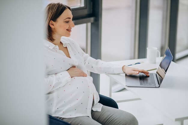 Jeune femme d'affaires enceinte travaillant sur ordinateur au bureau