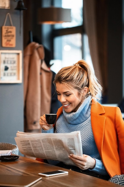 Photo gratuite jeune femme d'affaires heureuse lisant le journal quotidien et buvant du café après le travail dans un café