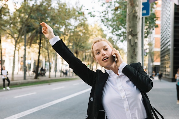 Photo gratuite jeune femme d'affaires levant la main pour arrêter la voiture sur la route de la ville