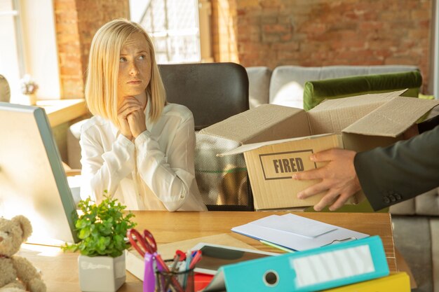 Jeune femme d'affaires licenciée, a l'air bouleversée. Doit emballer ses affaires de bureau et quitter le lieu de travail pour un nouveau travailleur. Problèmes de travail, stress, chômage, nouveau mode de vie ou fin de carrière.