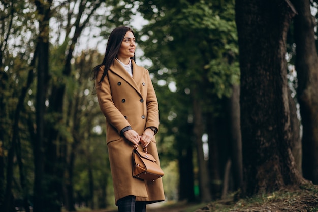 Jeune femme d'affaires en manteau marchant dans le parc