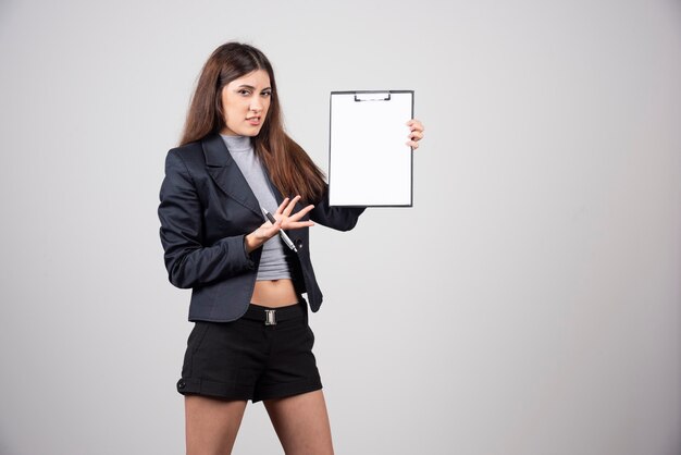 Une jeune femme d'affaires pointant sur le presse-papiers isolé sur un mur gris.