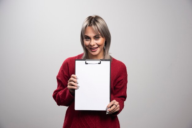 Jeune femme d'affaires avec presse-papiers vide sur fond gris.