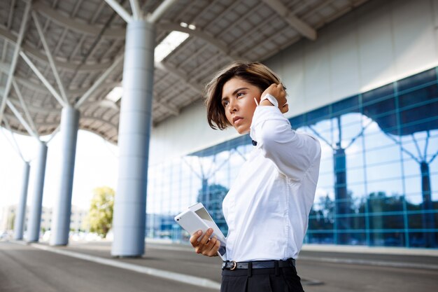 Jeune femme d'affaires prospère, parlant au téléphone, debout près du centre d'affaires.