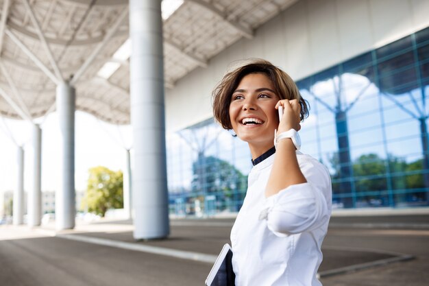 Jeune femme d'affaires prospère, parlant au téléphone, debout près du centre d'affaires.