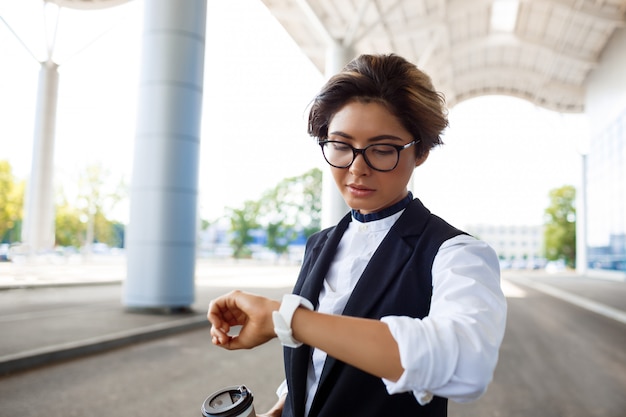 Jeune femme d'affaires prospère regardant la montre, debout près du centre d'affaires