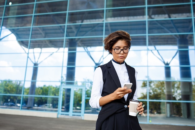 Jeune femme d'affaires prospère, regardant le téléphone, debout près du centre d'affaires.