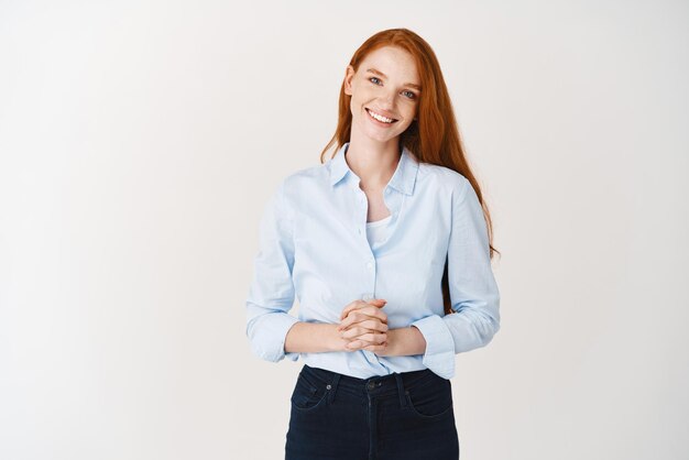 Jeune femme d'affaires rousse ressemblant à un client d'écoute amical et souriant professionnel debout sur fond blanc