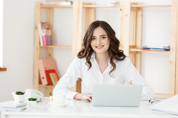 Jeune femme d'affaires ou secrétaire assis au bureau et travaillant souriant et regardant la caméra