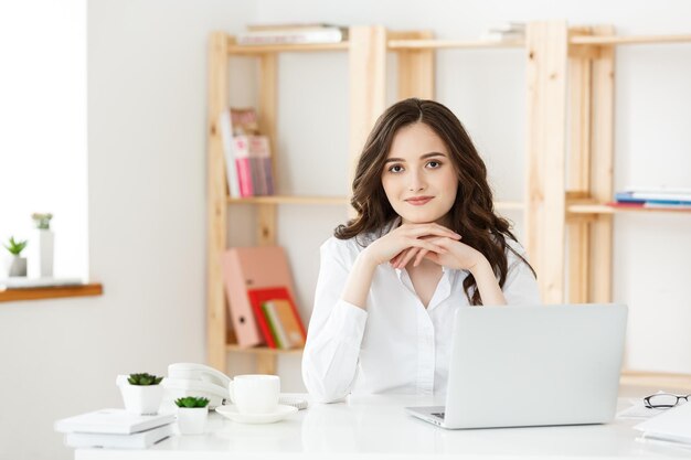 Jeune femme d'affaires ou secrétaire assis au bureau et travaillant souriant et regardant la caméra