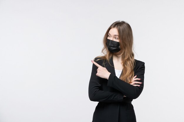 Jeune femme d'affaires sérieuse en costume portant un masque médical et pointant quelqu'un sur le côté droit sur un mur blanc isolé