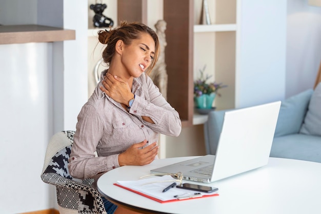 Jeune femme d'affaires souffrant de maux de cou massant son cou alors qu'elle était assise sur son lieu de travail au bureau à domicile