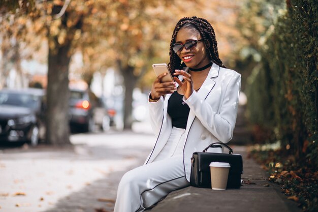 Jeune femme africaine, boire du café et à l'aide de téléphone