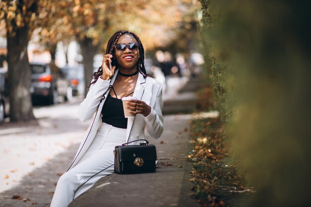 Jeune femme africaine, boire du café et à l'aide de téléphone