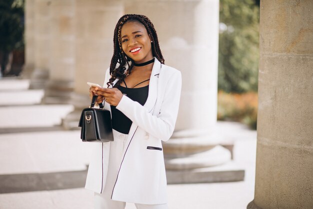 Jeune femme africaine en costume blanc à l'aide de téléphone