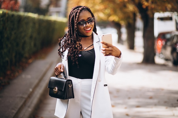 Jeune femme africaine en costume blanc à l'aide de téléphone