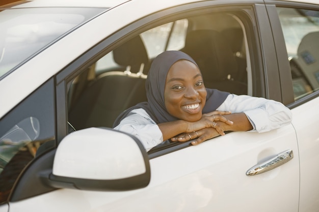 Jeune femme africaine musulmane pose avec les mains sur la ligne de fenêtre de voiture.