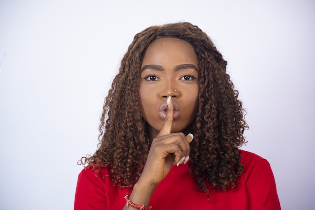 Jeune femme africaine avec son doigt sur sa bouche, faisant des gestes pour le silence