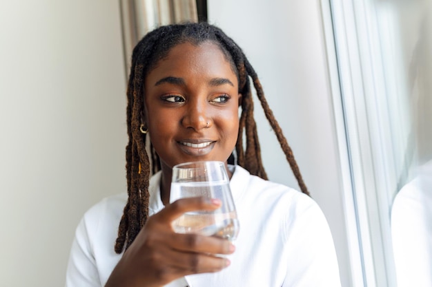 Jeune femme africaine en tenue décontractée buvant de l'eau du verre