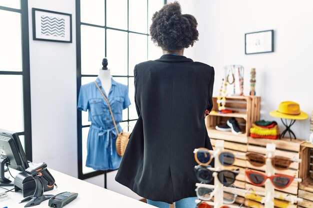 Jeune femme africaine travaillant comme gestionnaire dans une boutique de détail debout en arrière regardant loin avec les bras croisés