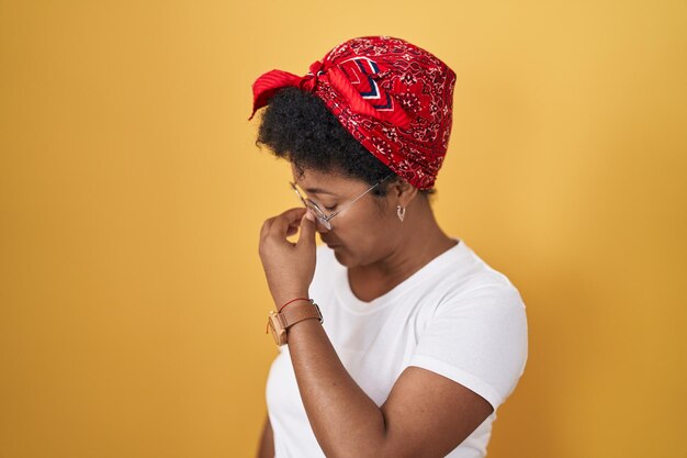 Jeune femme afro-américaine debout sur fond jaune fatigué se frottant le nez et les yeux ressentant de la fatigue et des maux de tête concept de stress et de frustration