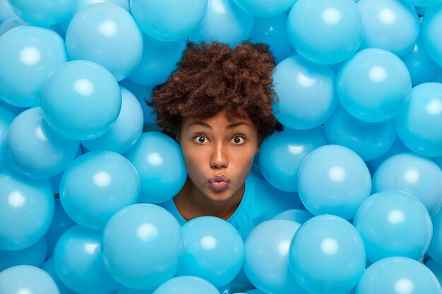 Jeune femme afro-américaine garde les lèvres arrondies pose autour de ballons gonflés bleus lors d'un événement festif