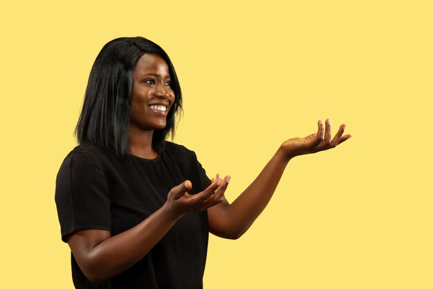 Jeune femme afro-américaine isolée sur fond de studio jaune, expression faciale. Beau portrait de femme demi-longueur. Concept d'émotions humaines, expression faciale. Choisir et inviter.