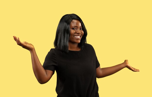 Jeune femme afro-américaine isolée sur mur jaune, expression faciale. Beau portrait de femme demi-longueur. Concept d'émotions humaines, expression faciale. Choisir et inviter.