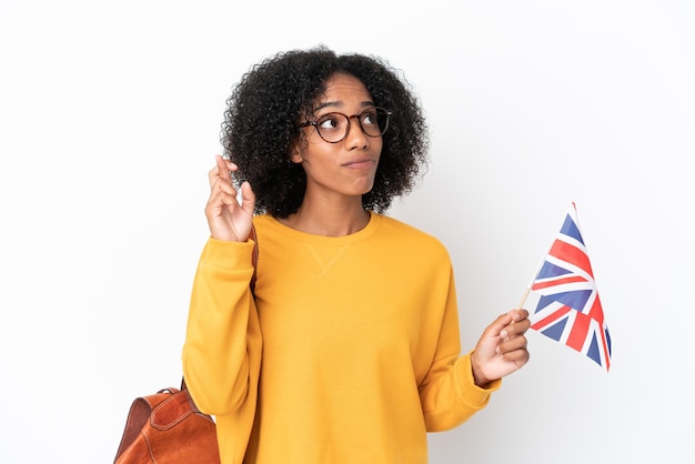 Jeune femme afro-américaine tenant un drapeau du royaume-uni isolé sur fond blanc avec les doigts croisés et souhaitant le meilleur